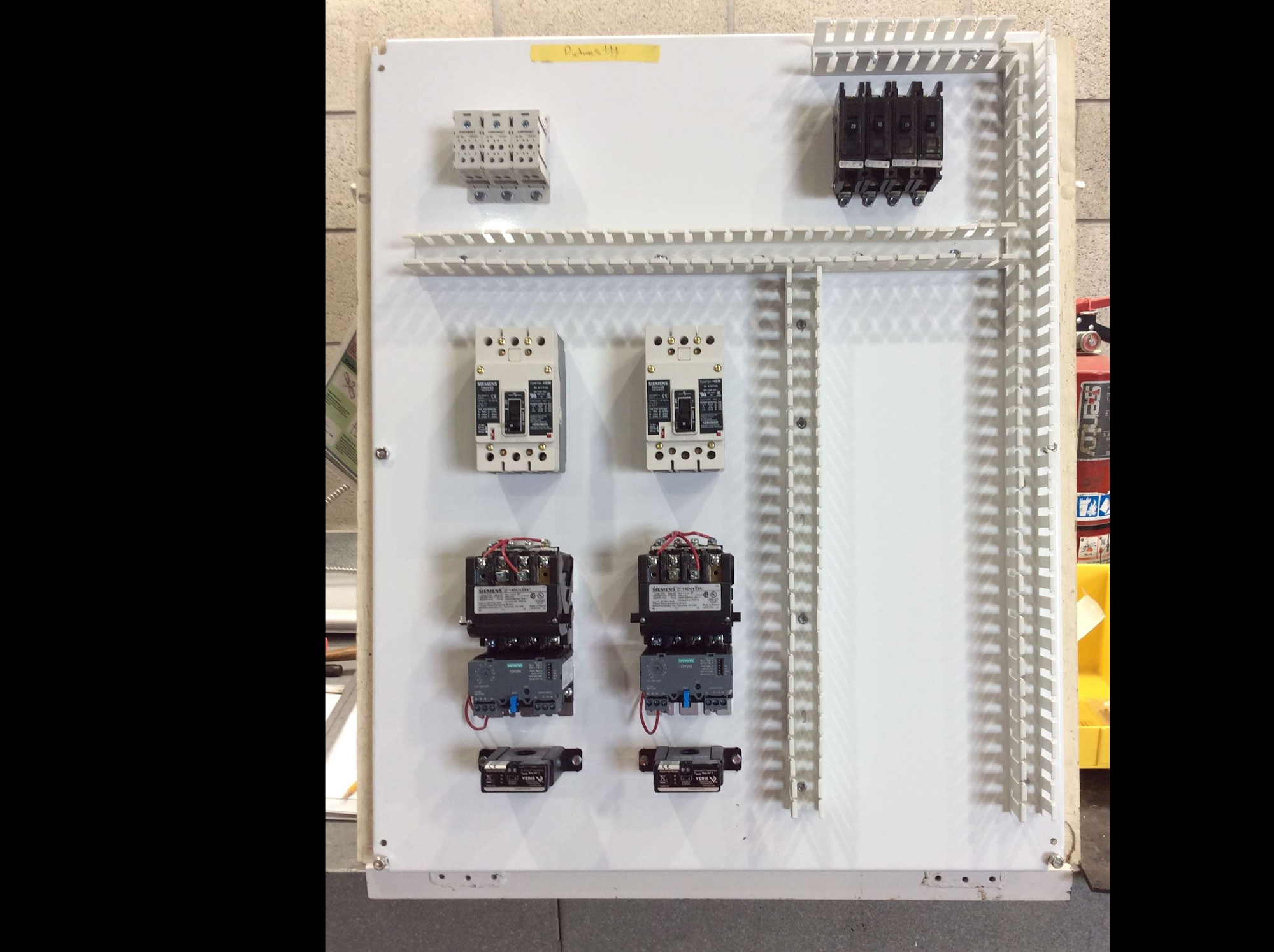 The image shows an electrical control panel with various relays and terminal blocks mounted on a white backplate.
