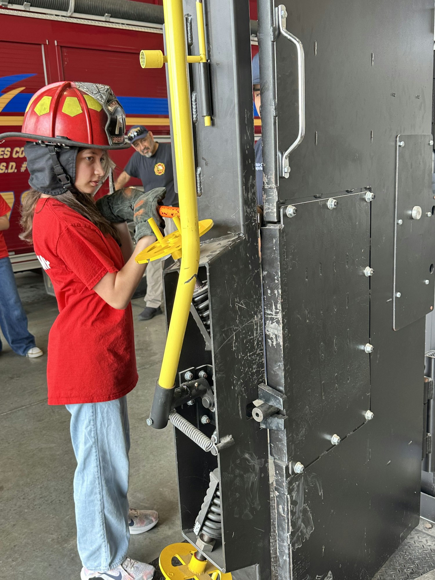 A person in a red shirt and helmet is interacting with a large black and yellow mechanical structure.
