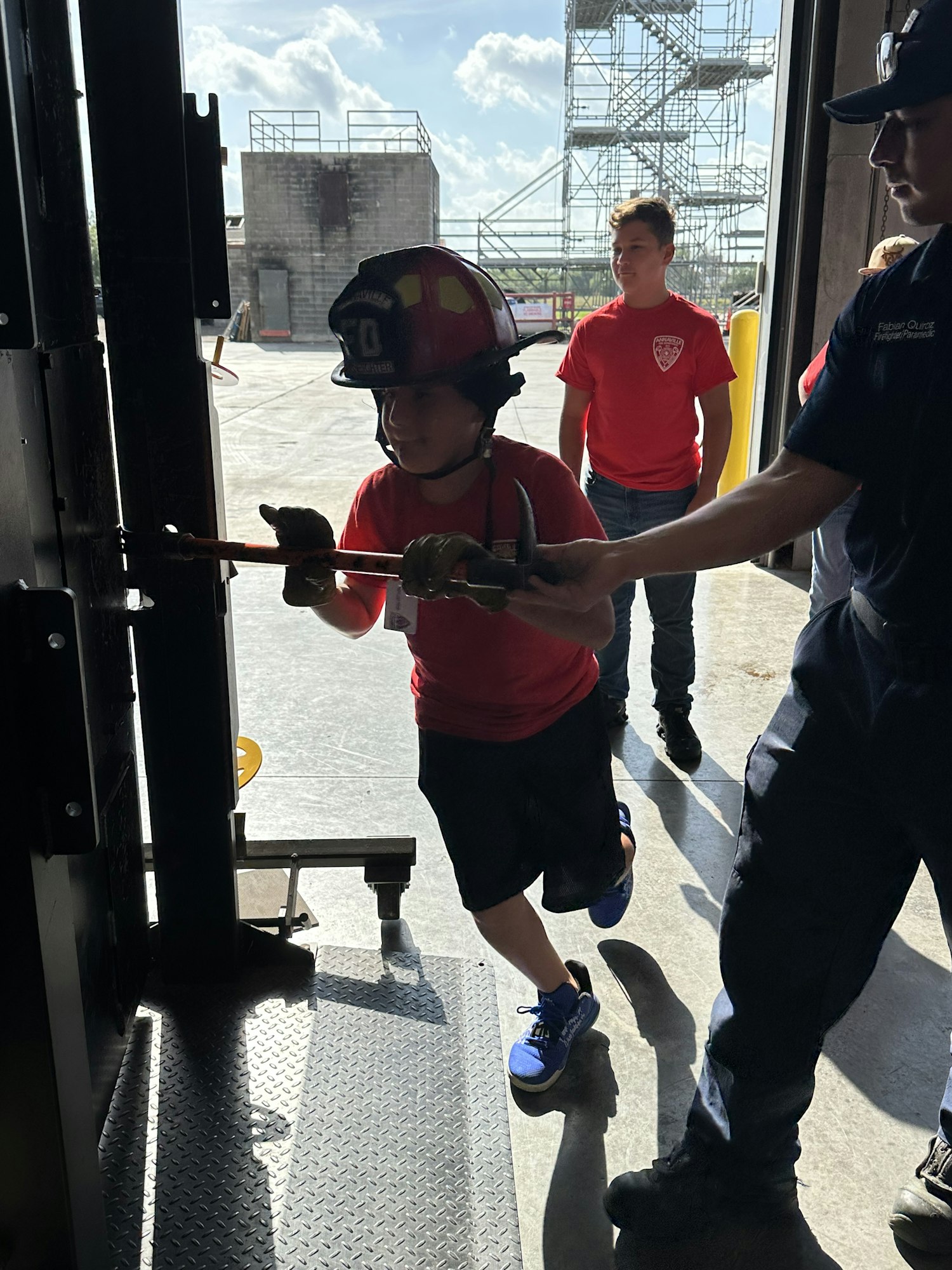 Firefighter trainees practicing door breaching techniques outdoors, using tools in a training facility.