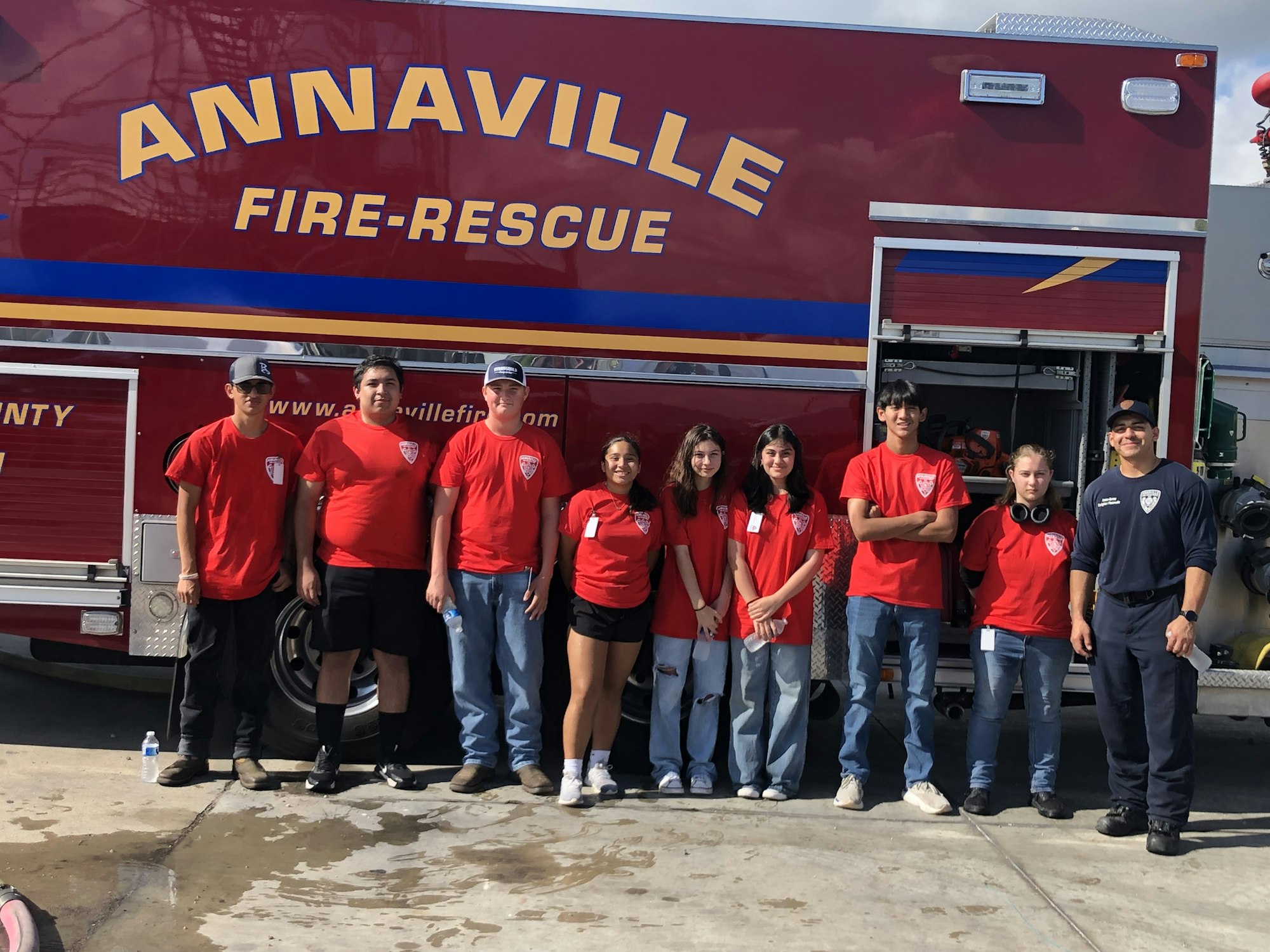 A group of people in red and blue shirts standing in front of a fire-rescue truck with "ANNAVILLE FIRE-RESCUE" on it.