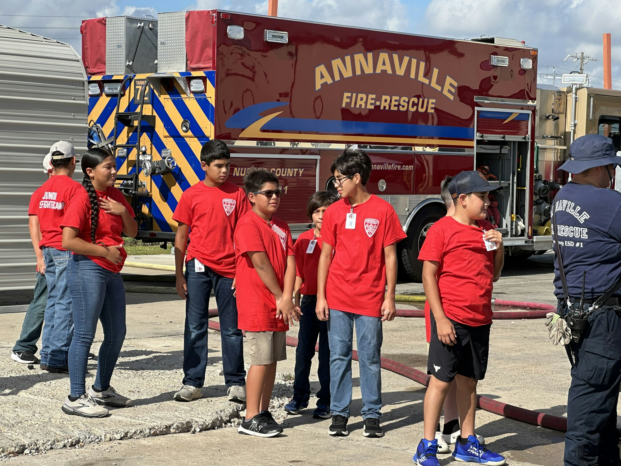A group of kids in red shirts marked "Junior Firefighter" stands near an Annaville fire-rescue truck.