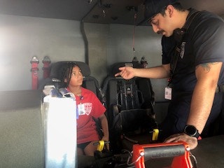 A firefighter is talking to a child sitting inside a fire truck, engaging in a friendly conversation.