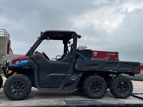 A six-wheeled off-road vehicle with a cargo bed is parked outside on a concrete surface.