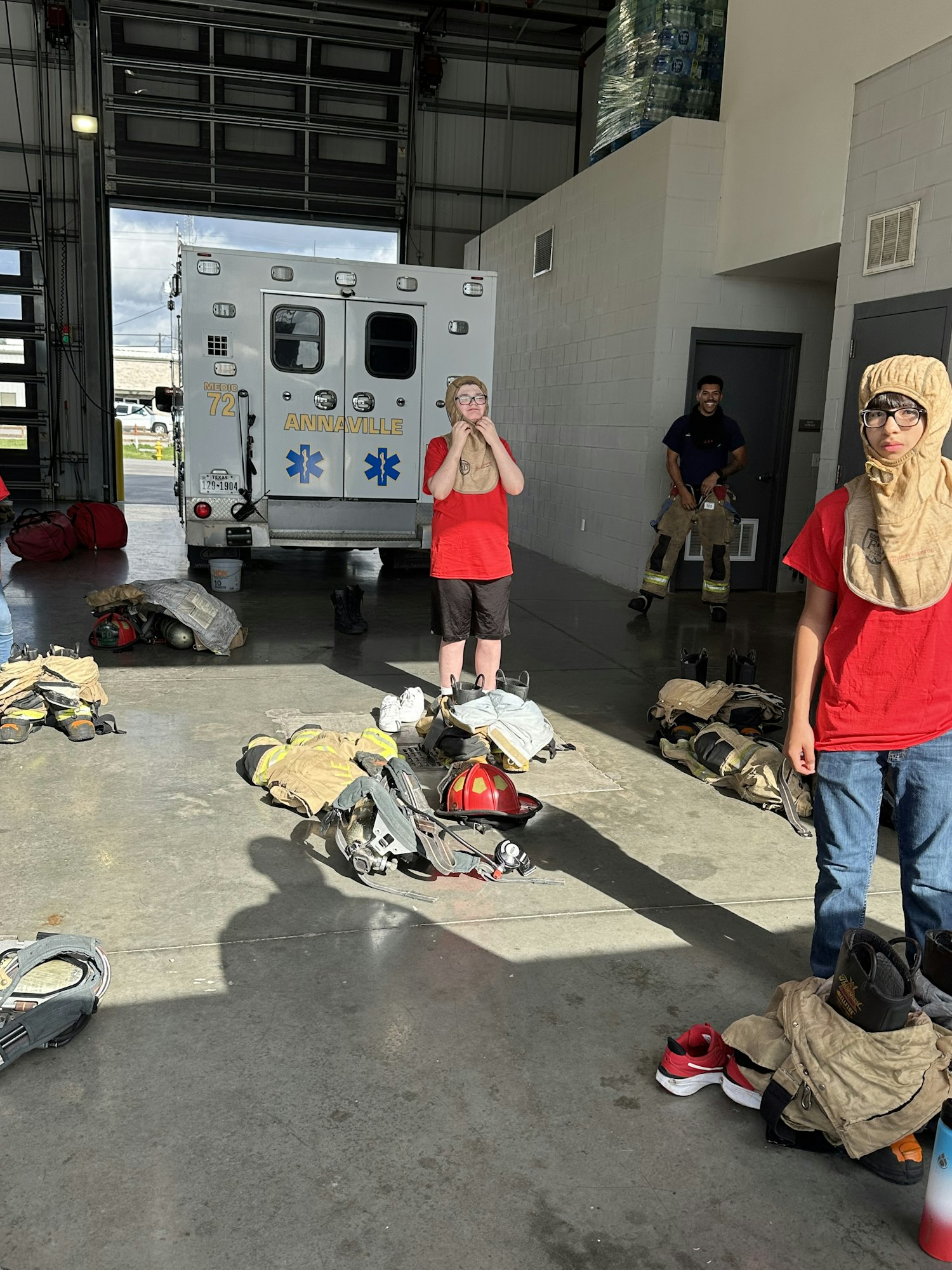 People in a garage near an ambulance with fire gear and water bottles in the background.