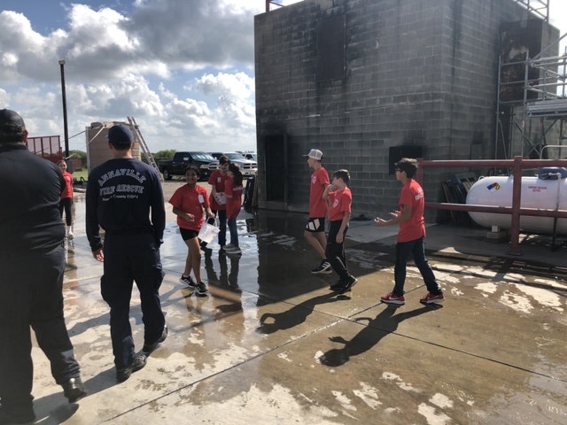 A group of people in red shirts and a firefighter enjoying outdoor water activities on a sunny day.