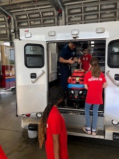 People, including children, are inside an ambulance at a fire station.