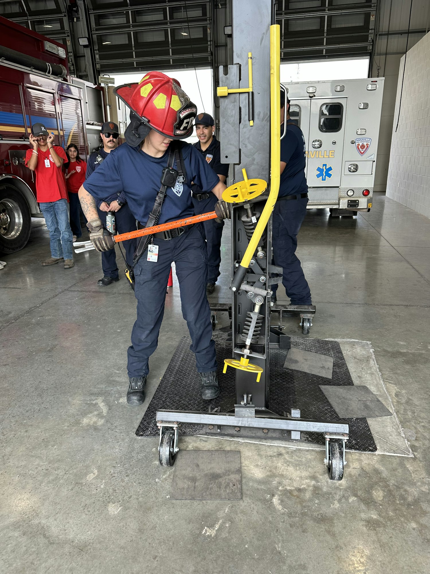 Firefighters maneuvering equipment inside a garage with an ambulance and a fire truck nearby.