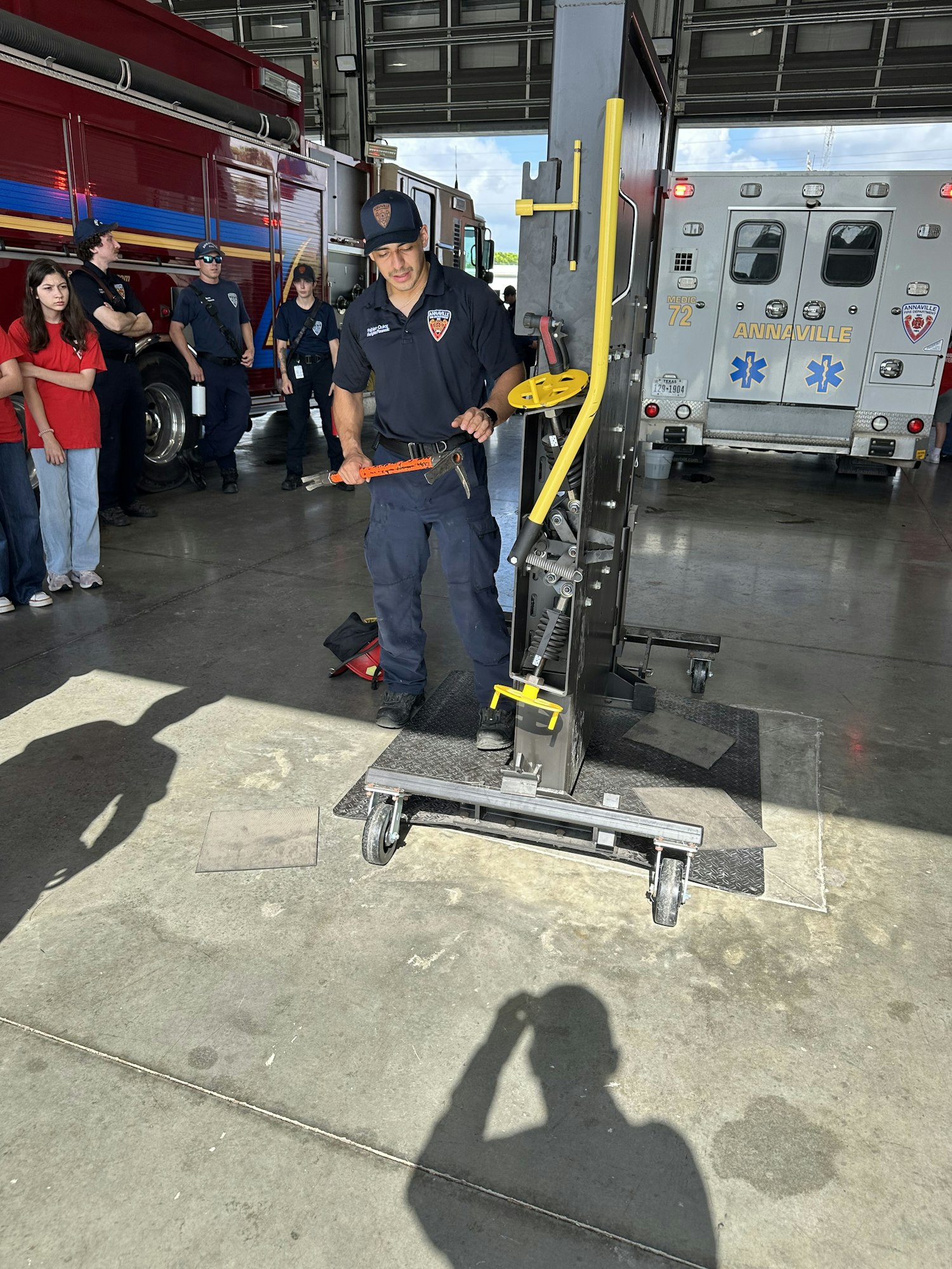 A firefighter demonstrating equipment beside an ambulance in a fire station.