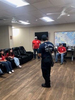A group of people in a room with maps and couches; some are standing, others seated.
