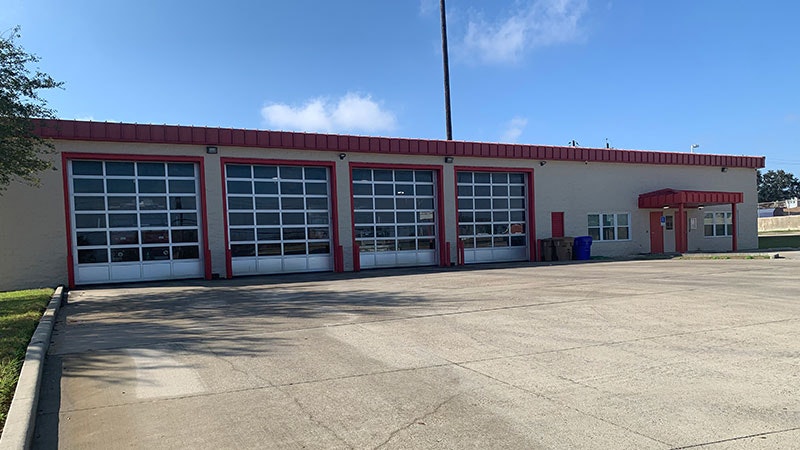 A building with four large garage doors, likely a fire station or vehicle facility, with a red and beige color scheme.