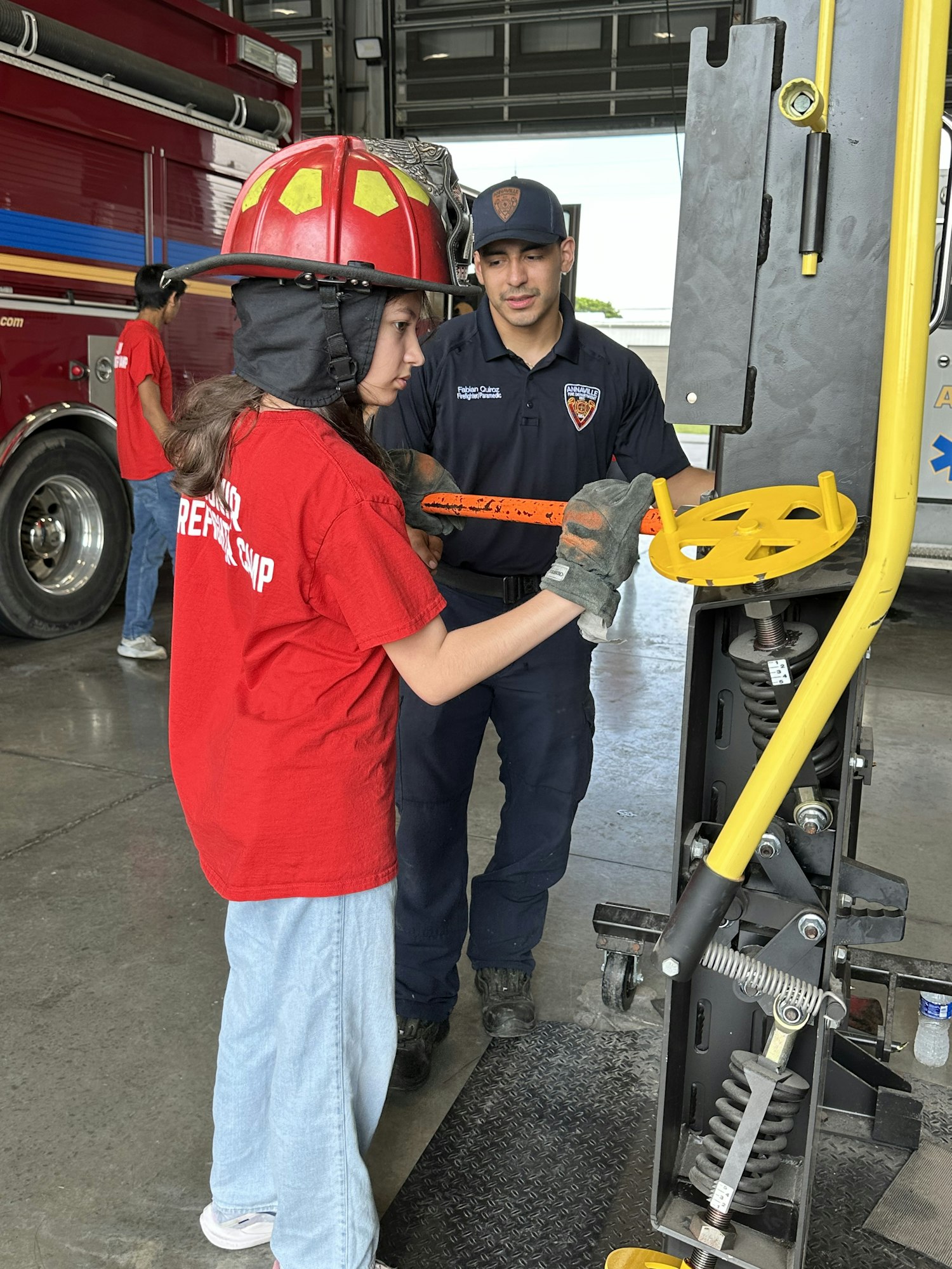 Two people in firefighting gear operate rescue equipment in a fire station.