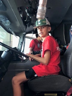 A person in a red shirt and cap sits inside a vehicle, smiling.