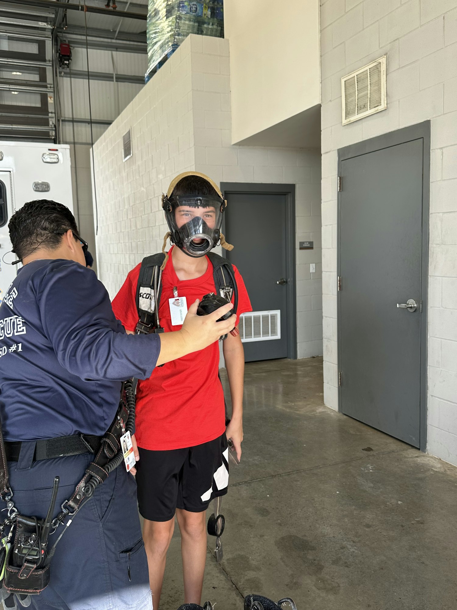 A person in a red shirt wearing a face mask is being assisted by another person indoors.