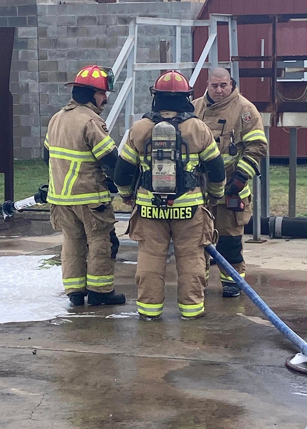 Three firefighters in gear, with hoses, standing outside near a building.