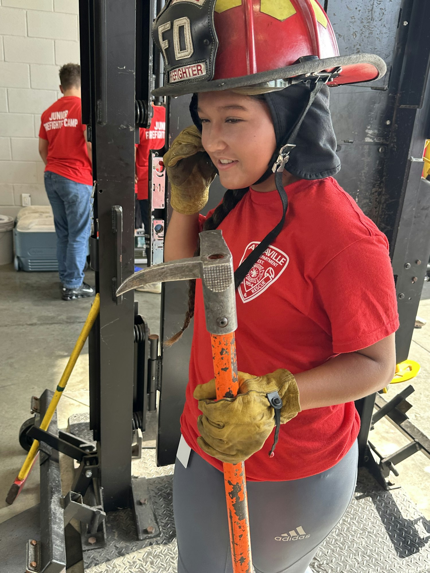 A person in firefighting gear using an orange tool. They wear a red helmet and gloves.