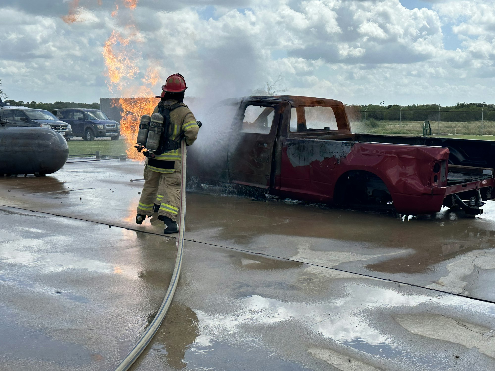 Firefighter extinguishing a burning red truck with flames and smoke rising from it.