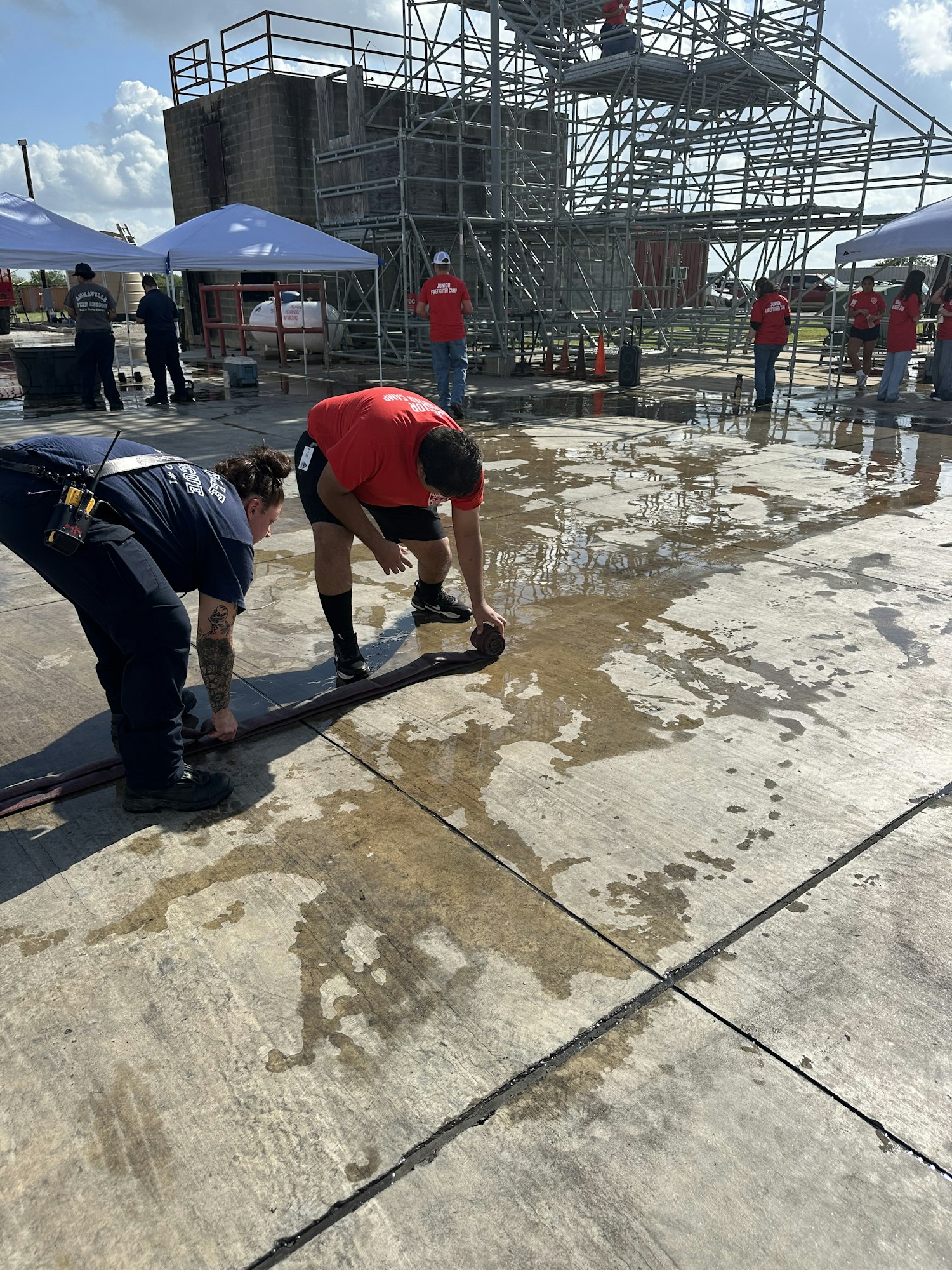 People are handling a heavy hose on a wet concrete surface near scaffolding.