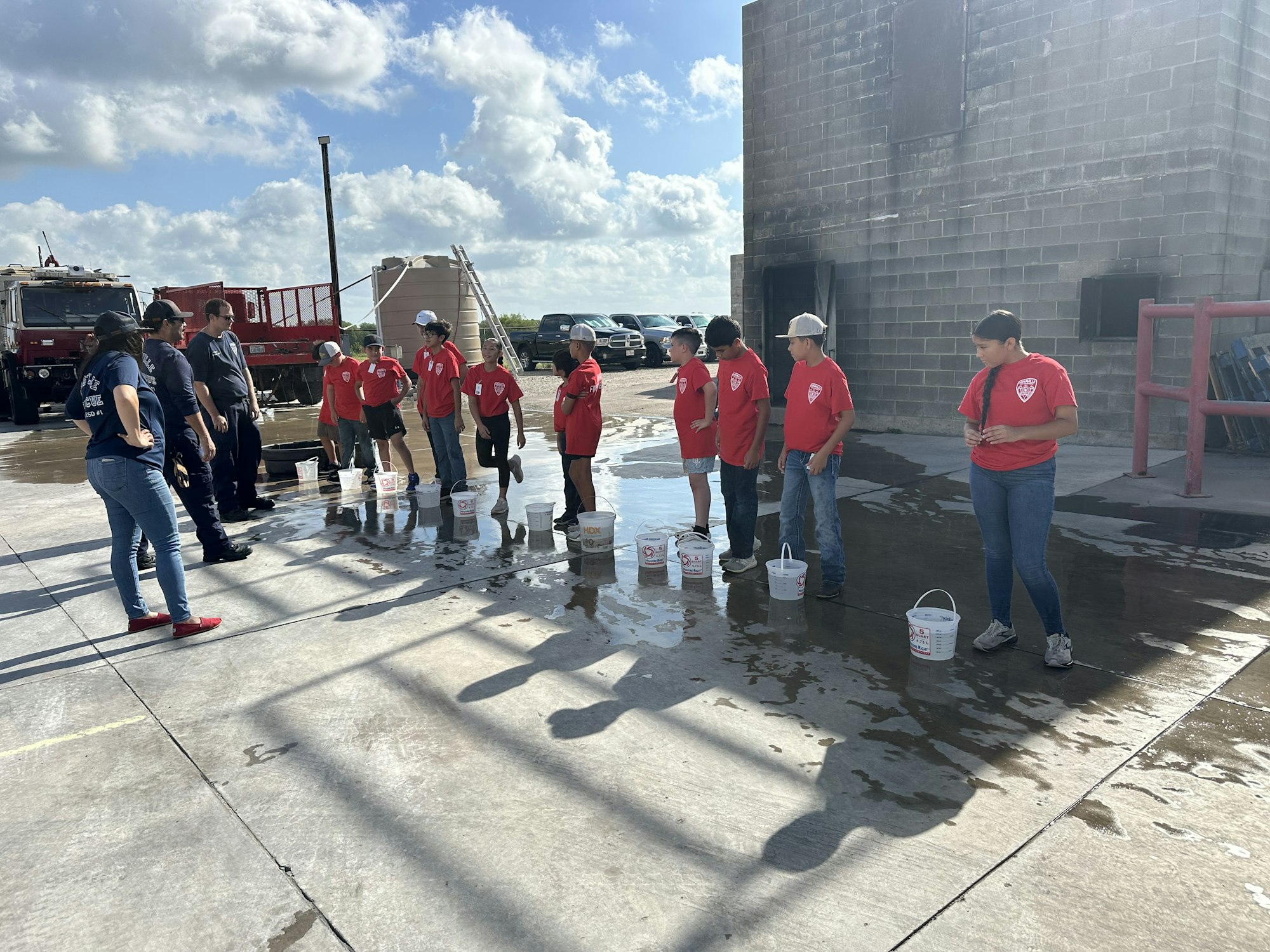 A group of people in red shirts stand in a line with buckets of water, possibly participating in a training or activity.