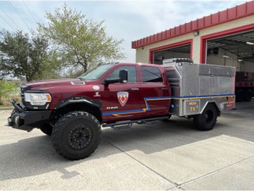 A red utility truck with off-road tires is parked in front of a fire station.