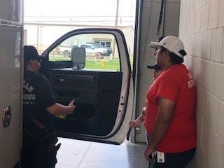 Three people near an open truck door inside a garage or facility.