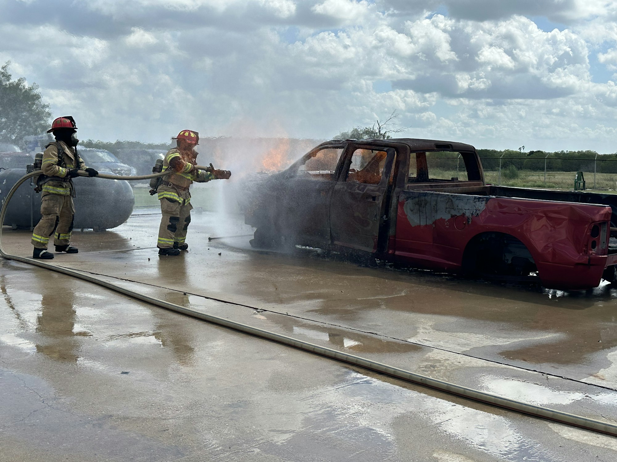 Firefighters extinguishing flames on a burning red pickup truck.