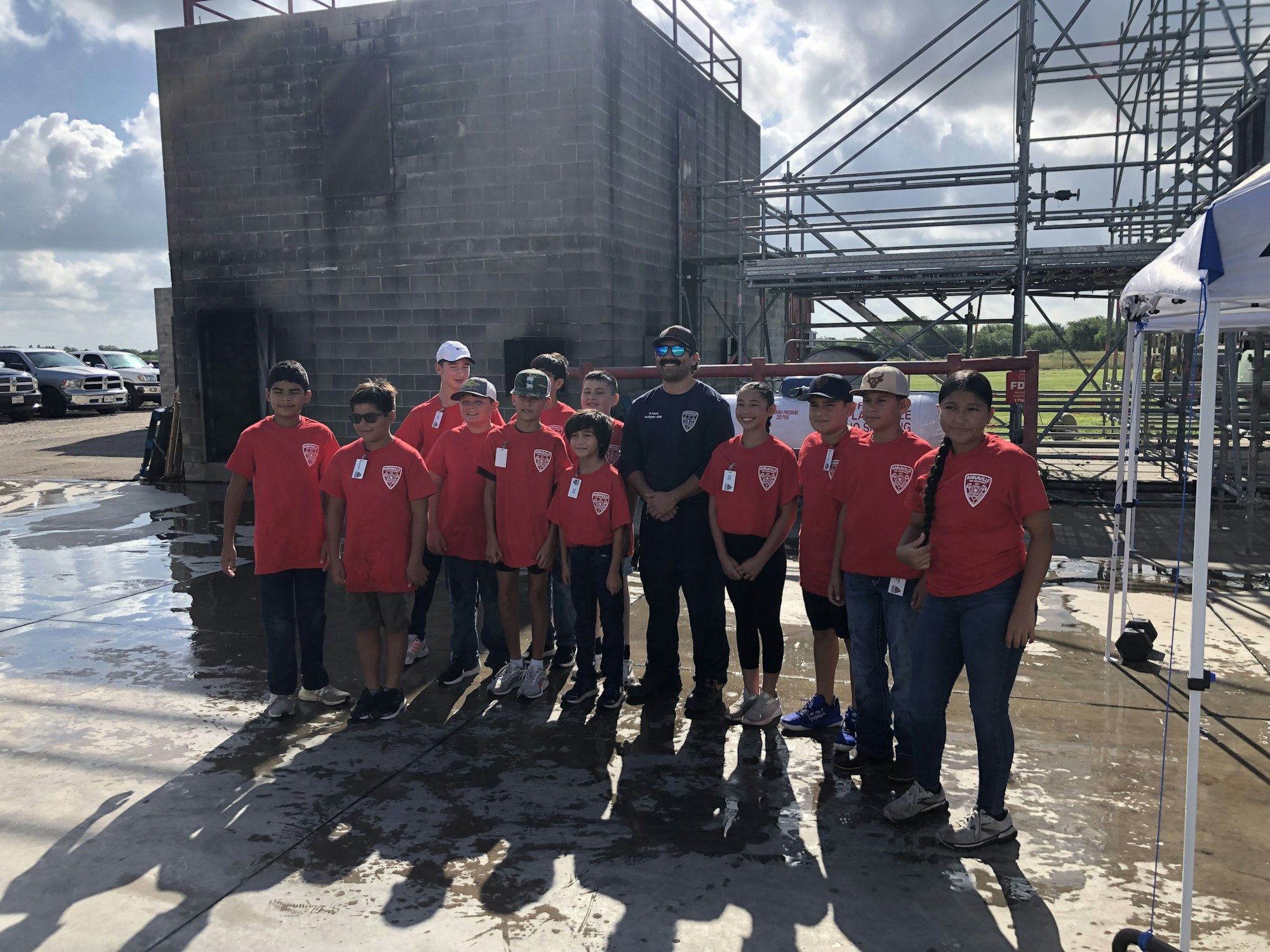 A group of people in matching red shirts and one in dark, standing outside near a building and scaffolding.