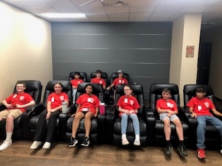 A group of kids in red shirts sitting in reclining chairs in a room.
