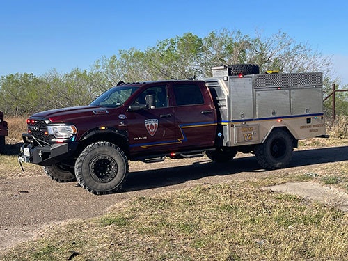 A maroon emergency response truck with all-terrain tires parked on a rural road.