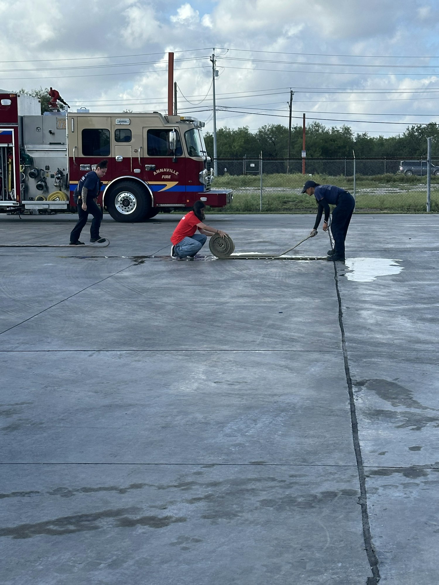 Firefighters are cleaning equipment near a fire truck on a concrete surface.