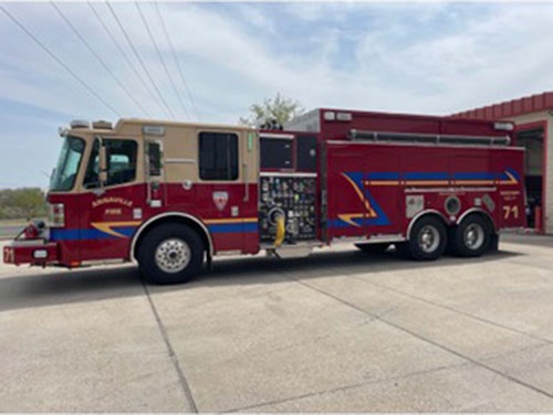 A red and beige fire truck parked outside a fire station.