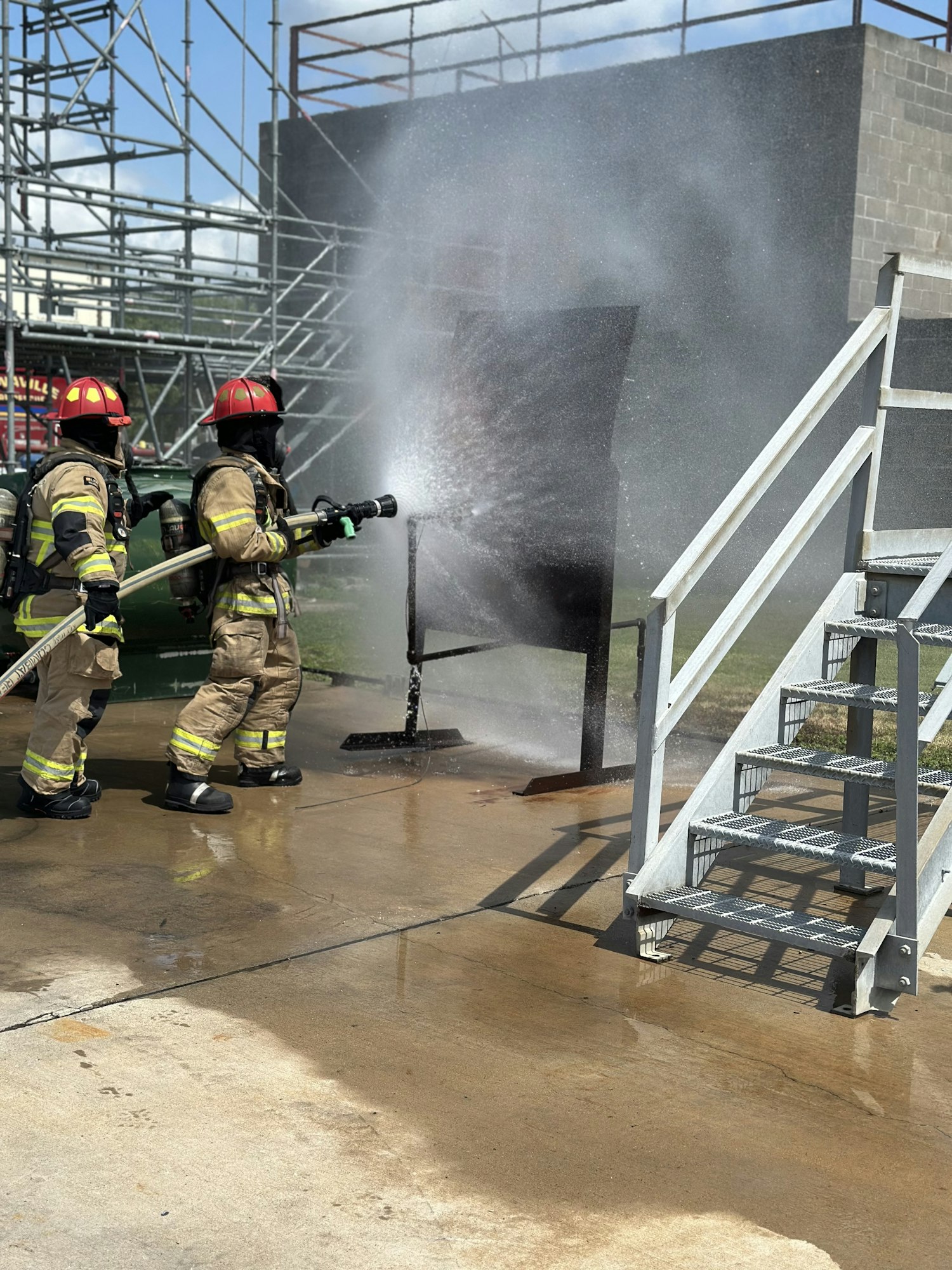 Two firefighters in gear spray water during a training exercise.