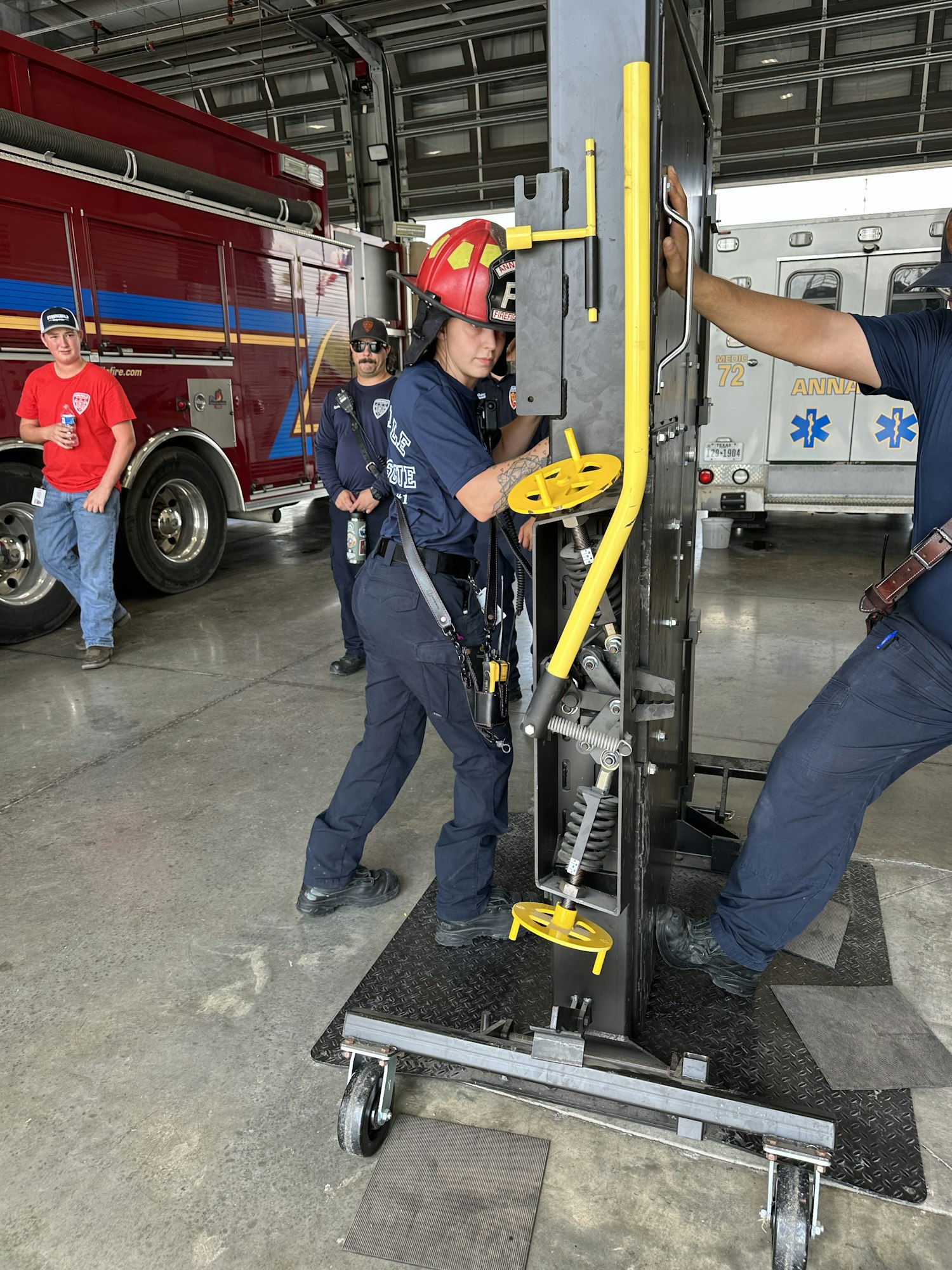 A group of firefighters operate equipment indoors, near a fire truck and ambulance.