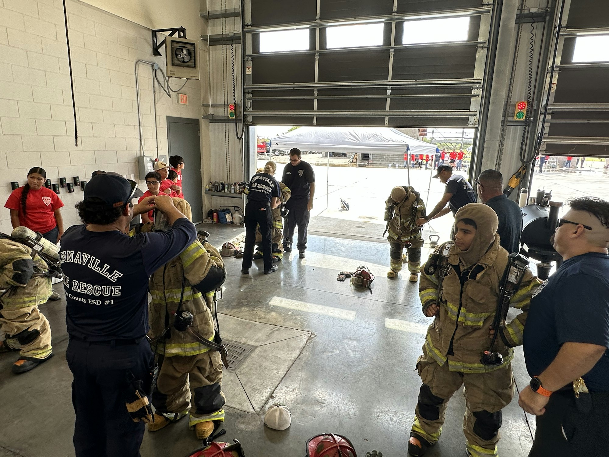 Firefighters in gear, preparing inside a garage. Training or drill with equipment and teamwork evident.