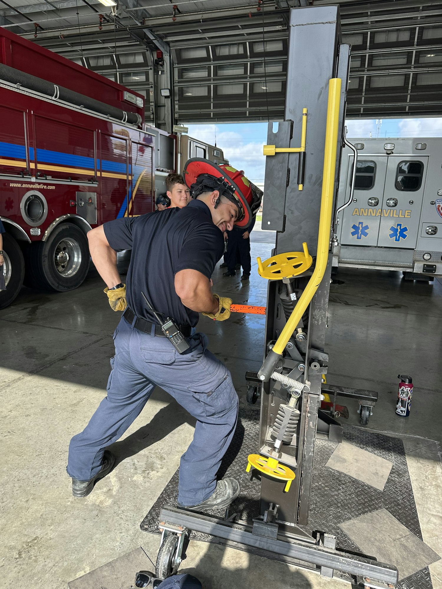 A firefighter in a garage operates equipment in front of a fire truck and ambulance.