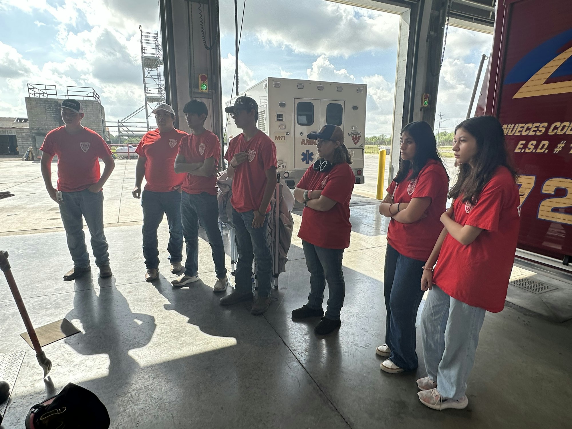 A group of people in red shirts standing inside a garage near an ambulance.