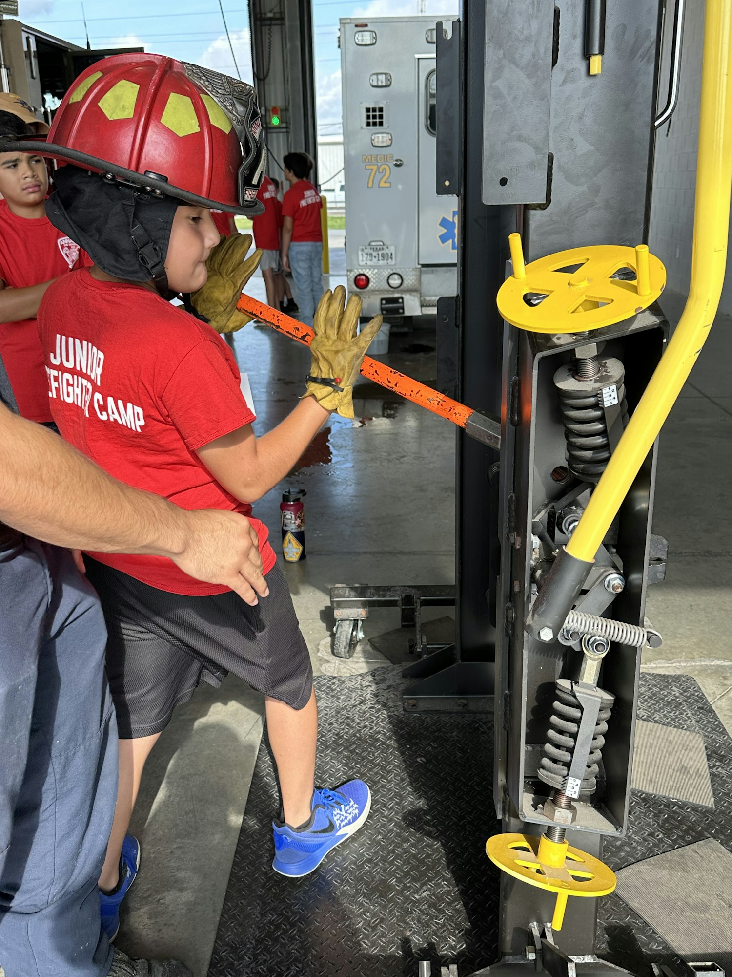 A child in a fire helmet operates a tool at a Junior Firefighter Camp.