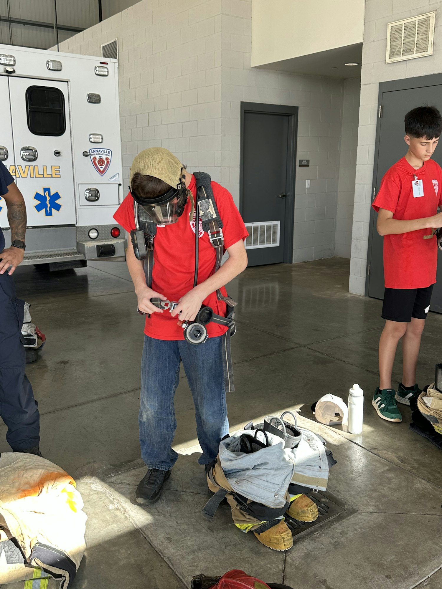 People in red shirts preparing fire-fighting gear beside an ambulance, with various protective clothing and equipment on the ground.