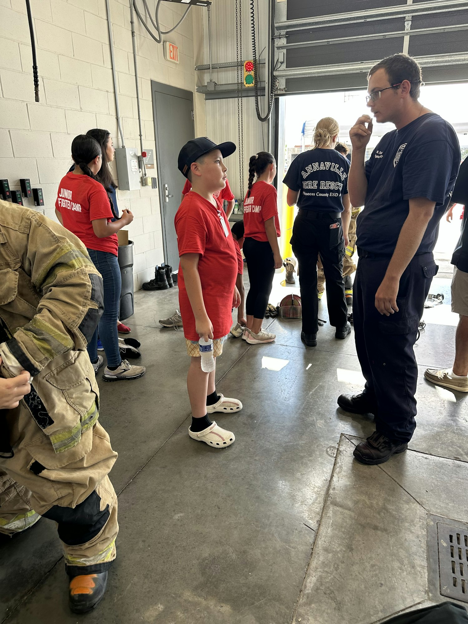 People wearing uniforms and casual clothes are gathered indoors, possibly in a garage or fire station setting.