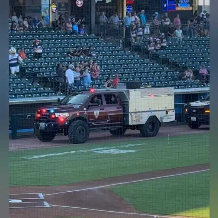 A fire truck and another emergency vehicle on a baseball field with spectators in the stands.