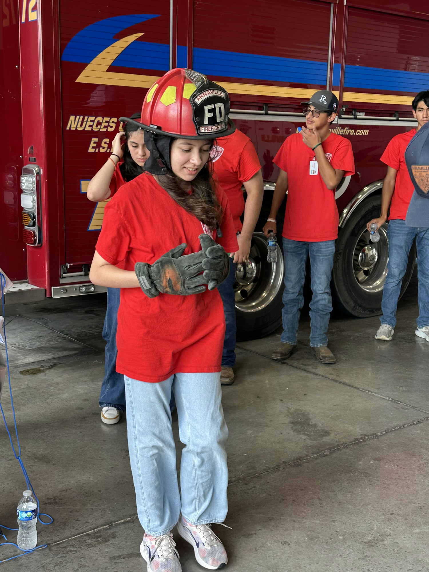 A group of people in red shirts, one wearing a firefighter helmet, stand near a fire truck.