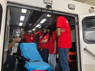 A group of people in red shirts stand inside an ambulance, gathered around a stretcher.