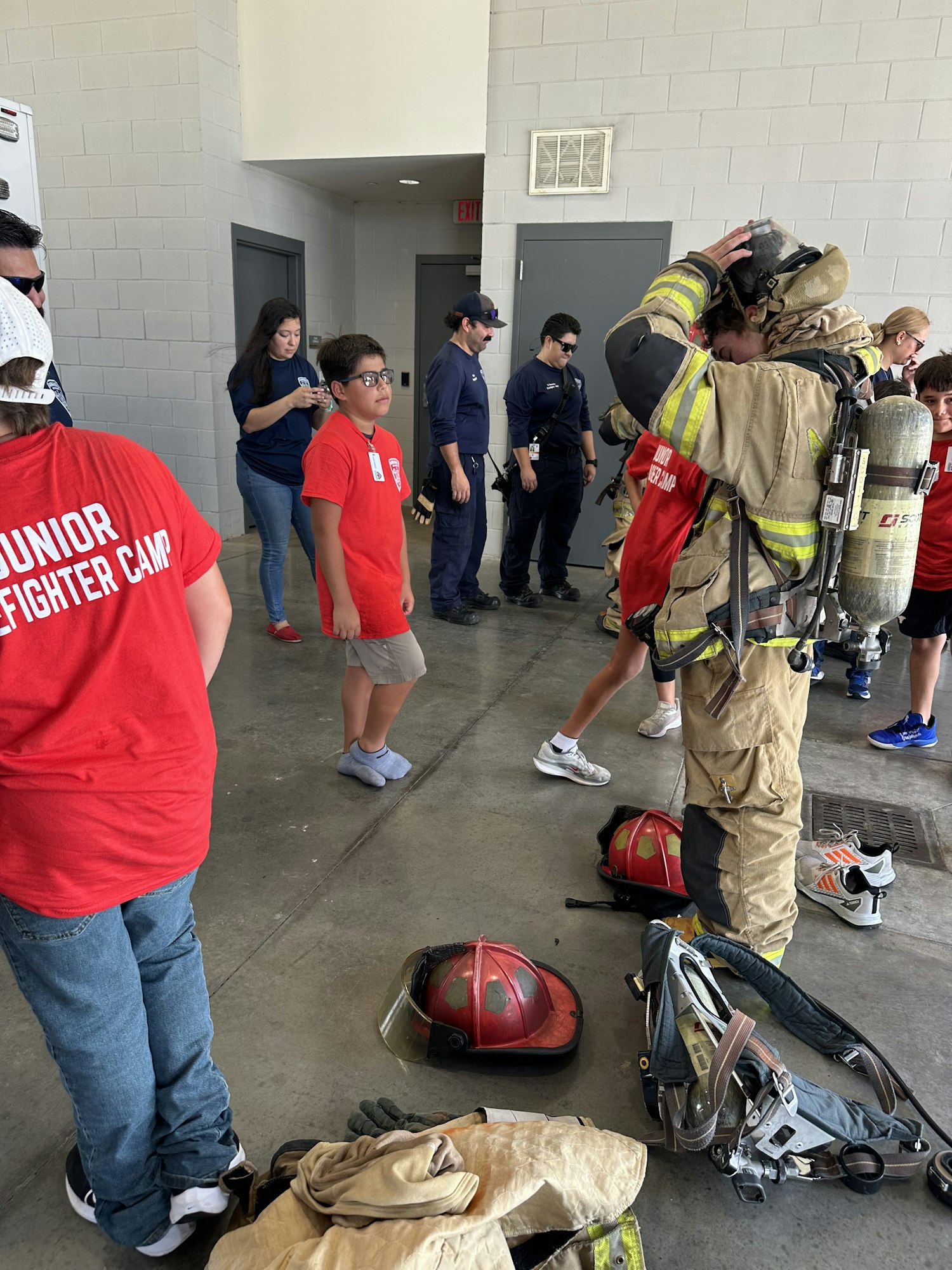A firefighter suits up while people watch during a junior firefighter camp event.