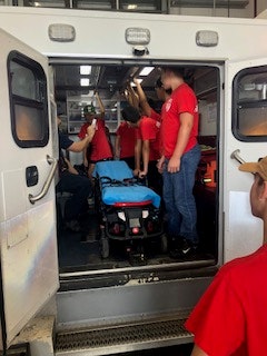 People in red shirts inside an ambulance with a stretcher.