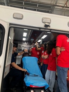 A group of people in red shirts are gathered around an open ambulance with a blue stretcher inside.