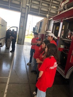 Group of people in red shirts inside a fire station, standing near a fire truck.