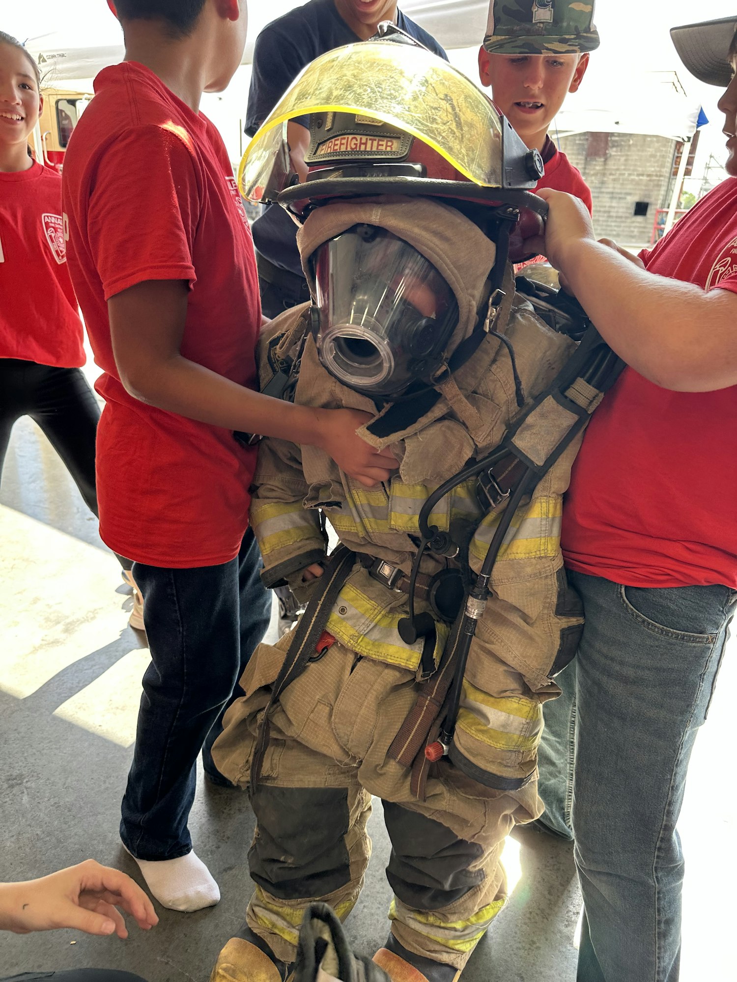 A person wearing a firefighter suit and helmet is being surrounded by others in red shirts, helping them.