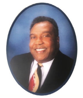 A smiling person wearing a suit and tie against a blue background, in an oval frame.