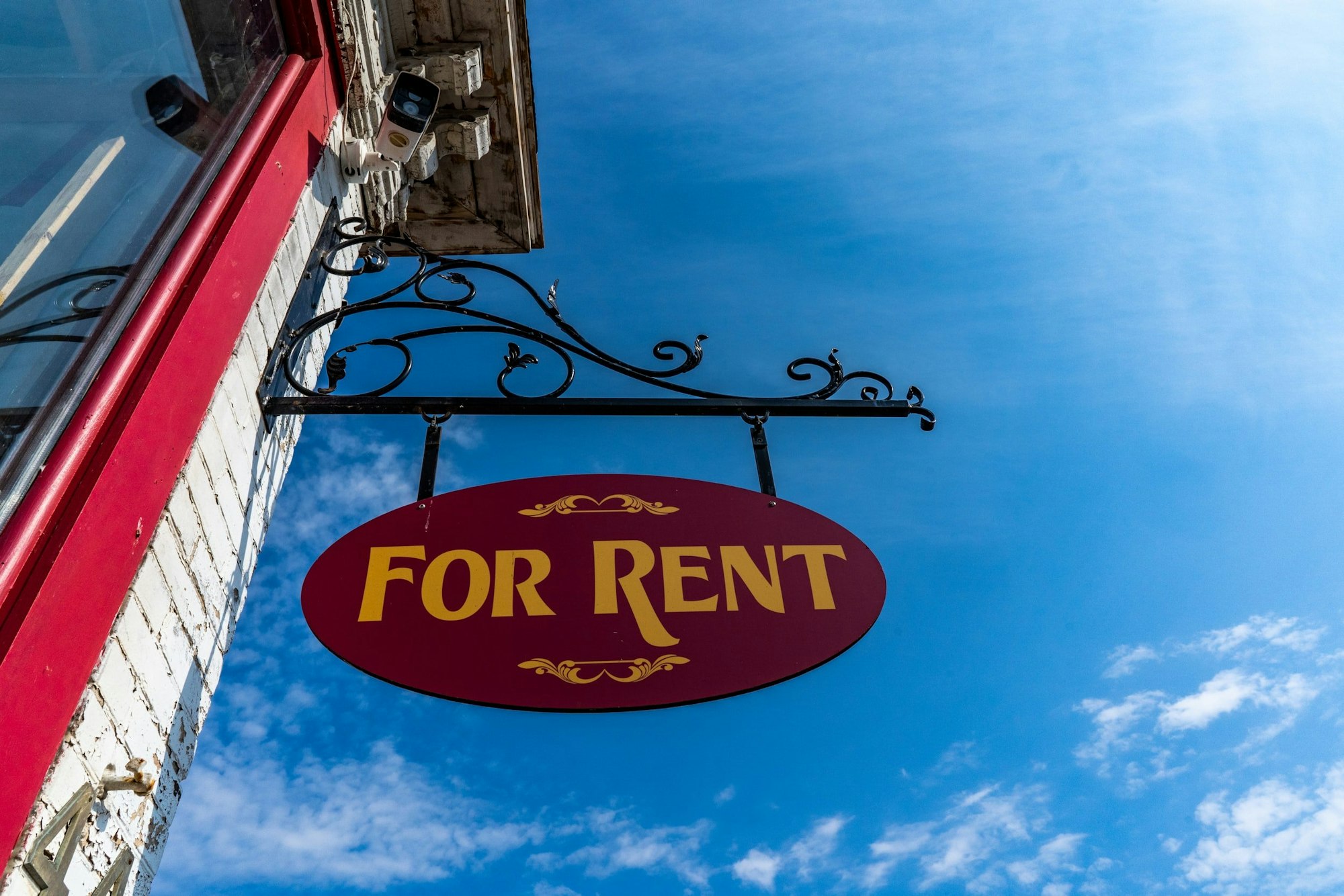"For Rent" sign hanging outside a building against a clear blue sky.