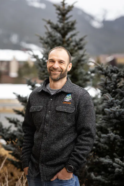 May contain: face, happy, head, person, smile, plant, tree, fir, clothing, coat, adult, male, man, photography, portrait, knitwear, sweater, jacket, jeans, and pants