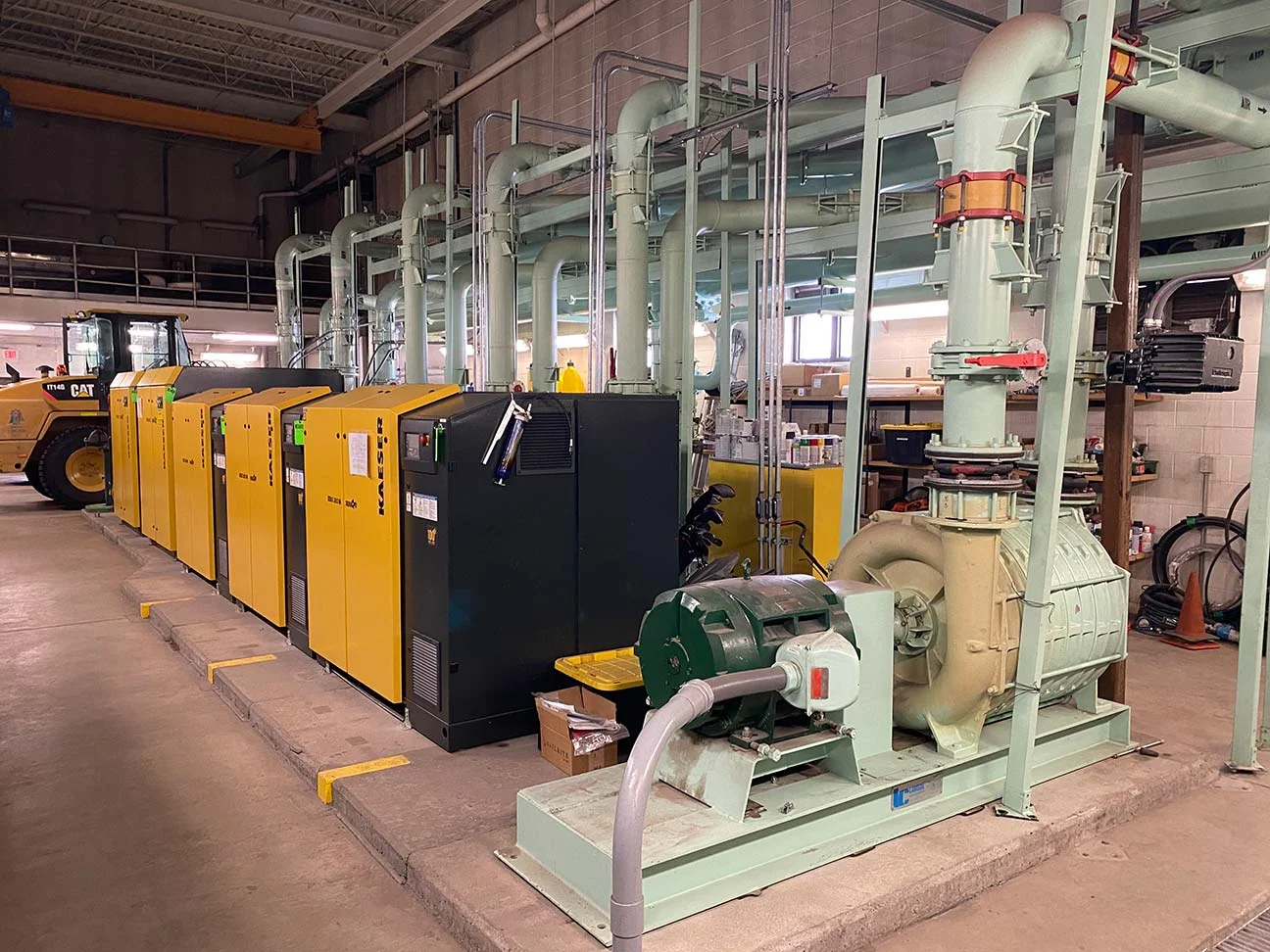 Industrial setting with a row of yellow power generators and a large green ventilation system.